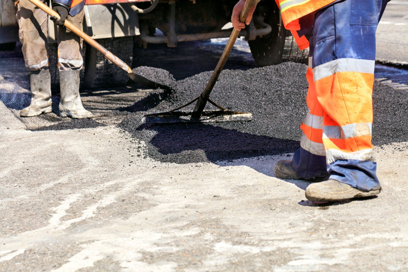 Road service worker shoveling new asphalt during construction and patching of a road